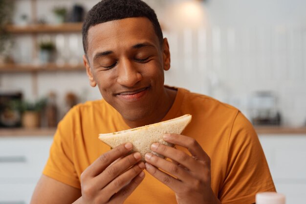 Retrato de un hombre afroamericano positivo con los ojos de sándwich cerrados disfrutando de comer