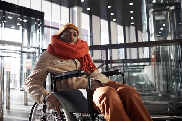 Retrato de hombre afroamericano en silla de ruedas mirando a la cámara al entrar en un centro comercial accesible o en la estación de metro
