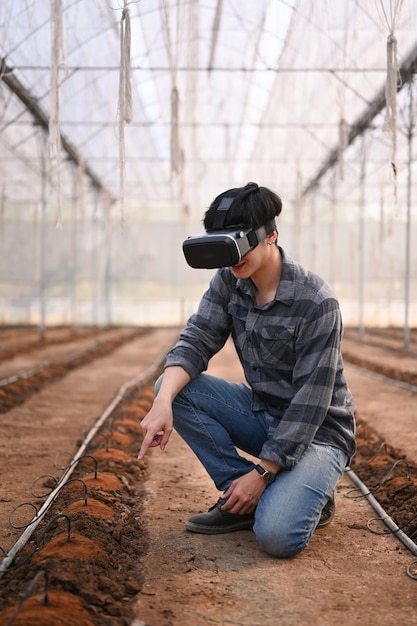 Retrato de hombre agricultor inteligente sentado en invernadero y con tecnología de gafas de realidad visual.