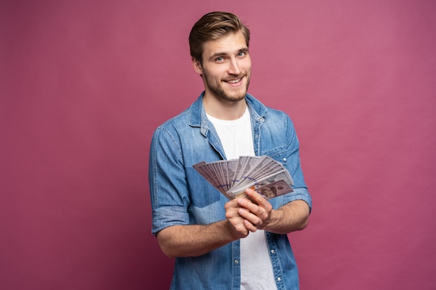 Foto retrato de un hombre alegre con billetes de un dólar sobre fondo rosa.