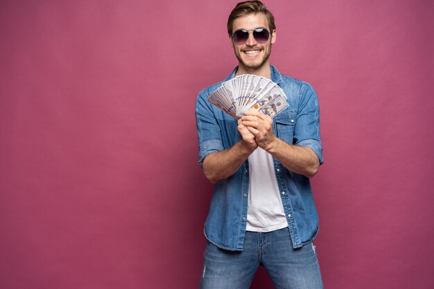 Retrato de un hombre alegre con billetes de un dólar sobre fondo rosa.