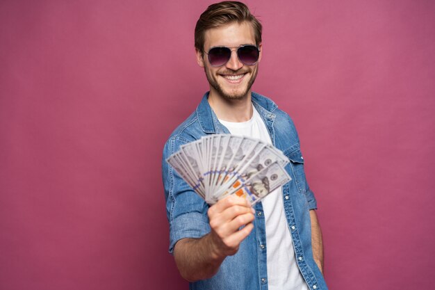 Retrato de un hombre alegre con billetes de un dólar sobre fondo rosa.