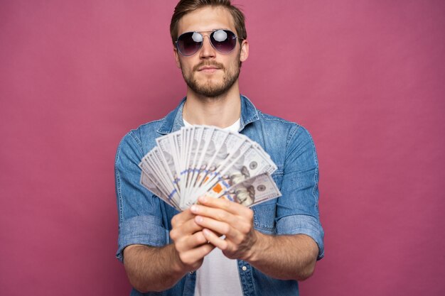 Retrato de un hombre alegre con billetes de un dólar sobre fondo rosa.