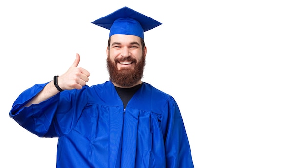 Retrato de hombre alegre estudiante con barba vistiendo soltero mostrando el pulgar hacia arriba