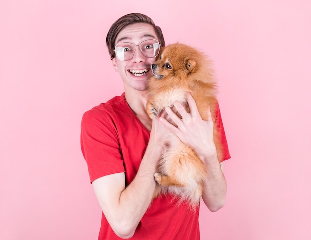 Retrato de un hombre alegre y guapo, usa gafas, una camiseta roja, sostiene un Pomerania, tiene una expresión alegre, posa con un espacio vacío de copia. Animales y amistad