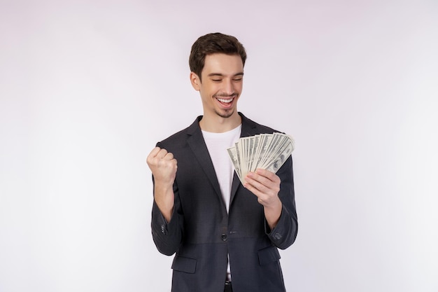 Foto retrato de un hombre alegre que sostiene billetes de dólar y hace gesto de ganador apretando el puño sobre fondo blanco.