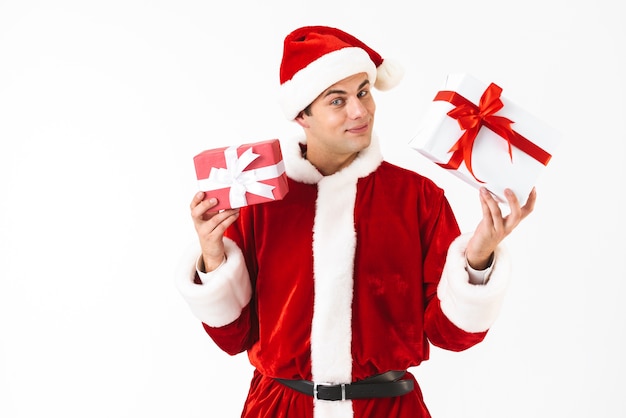 Retrato de hombre amable de 30 años en traje de santa claus y sombrero rojo con cajas de regalo