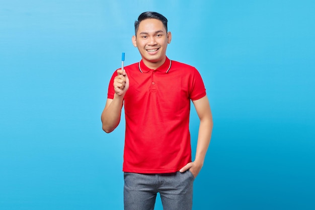Retrato de un hombre asiático adulto con camisa roja sonriendo alegremente después de tener una nueva idea y mirando la cámara aislada en el fondo azul
