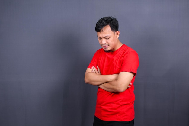 Retrato de hombre asiático atractivo en camiseta roja de pie con los brazos cruzados aislado fondo gris