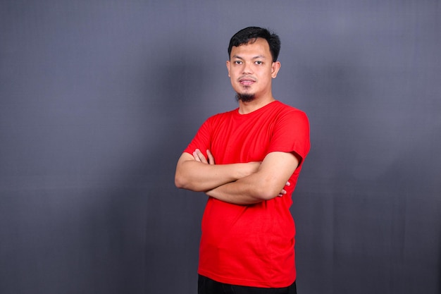 Retrato de hombre asiático atractivo en camiseta roja de pie con los brazos cruzados aislado fondo gris