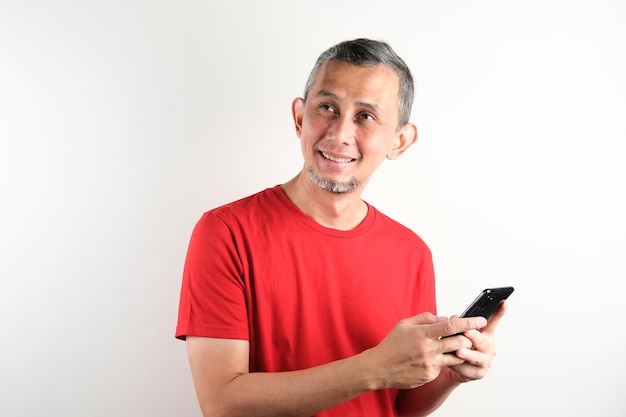 Retrato de hombre asiático con gafas y camisa roja posa feliz con la mano sosteniendo el celular