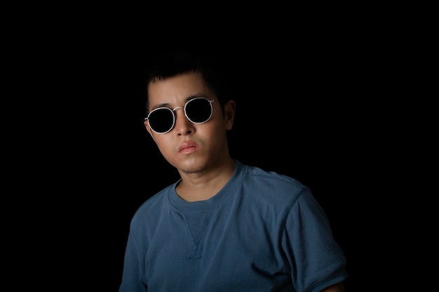 Retrato de un hombre asiático con gafas de sol con una camiseta azul sobre fondo negro