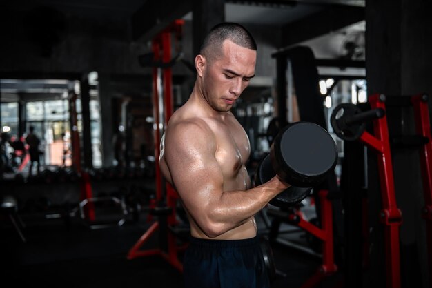 Retrato de hombre asiático con grandes músculos en el gimnasioGente de TailandiaEntrenamiento para una buena saludEntrenamiento de peso corporalFitness en el concepto de gimnasioBroma a los músculos abdominalesLevantar la pesa