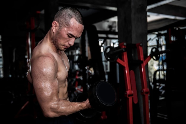 Retrato de hombre asiático con grandes músculos en el gimnasioGente de TailandiaEntrenamiento para una buena saludEntrenamiento de peso corporalFitness en el concepto de gimnasioBroma a los músculos abdominalesLevantar la pesa