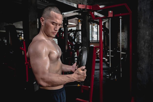 Retrato de hombre asiático con grandes músculos en el gimnasioGente de TailandiaEntrenamiento para una buena saludEntrenamiento de peso corporalFitness en el concepto de gimnasioBroma a los músculos abdominalesLevantar placa de acero pesado