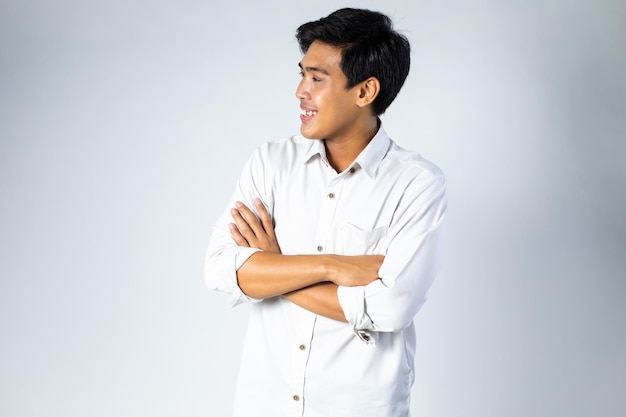 Retrato de hombre asiático joven emocionado y feliz manteniendo los brazos cruzados y sonriendo sobre fondo gris