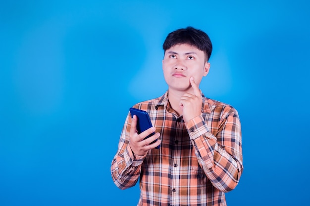Retrato de un hombre asiático joven y guapo con una camisa a rayas pensando sobre fondo azul