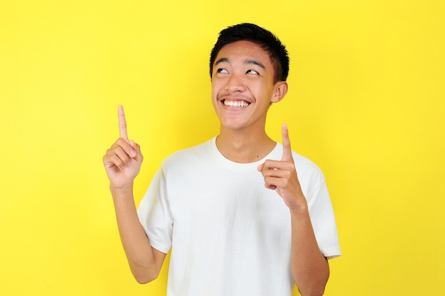 Retrato de hombre asiático joven inteligente y feliz pensando y mirar hacia arriba. Feliz joven asiático con camiseta blanca pensando y mirar hacia arriba, sobre fondo amarillo