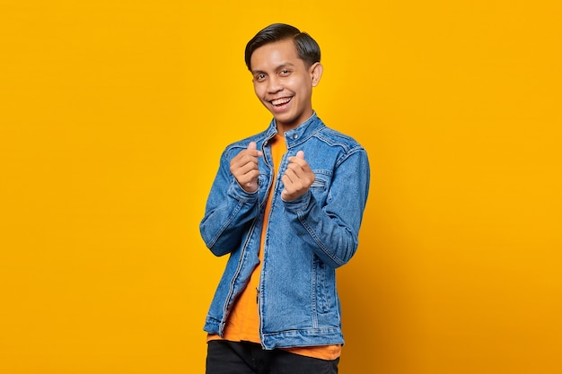 Retrato del hombre asiático joven sonriente que muestra el corazón del dedo sobre fondo amarillo