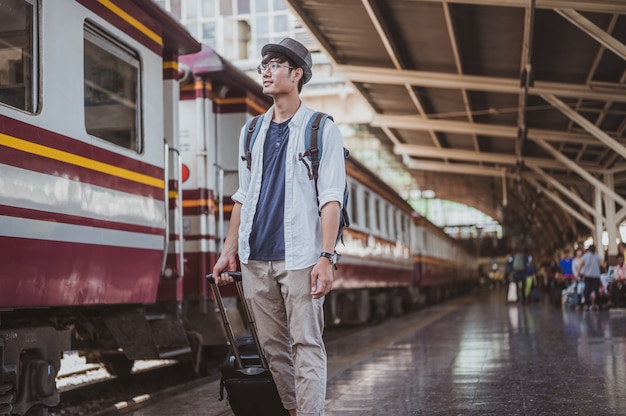 Retrato de hombre asiático llevando su equipaje en la estación de tren. Concepto de viaje. Turista hombre viajero caminando en la estación de tren.