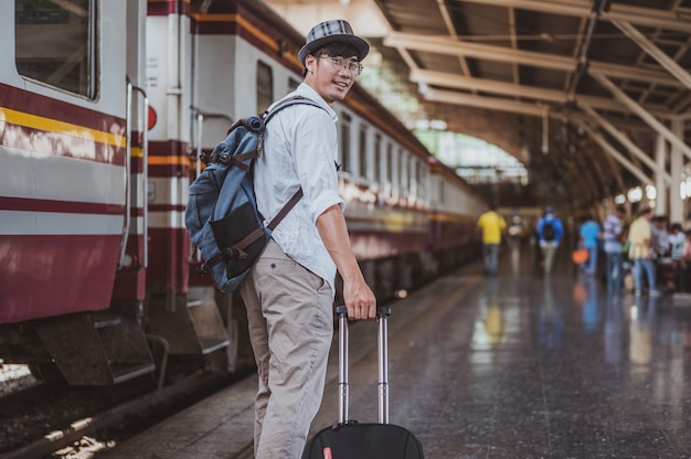 Retrato de hombre asiático llevando su equipaje en la estación de tren. Concepto de viaje. Turista hombre viajero caminando en la estación de tren.