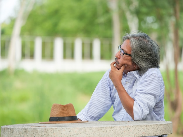 Retrato del hombre asiático mayor que se sienta solamente en jardín.