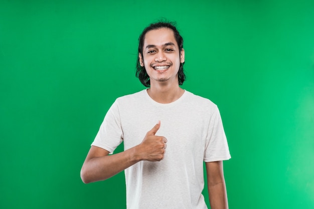 Retrato de hombre asiático mostrando los pulgares a la cámara con una sonrisa, aislado sobre fondo verde