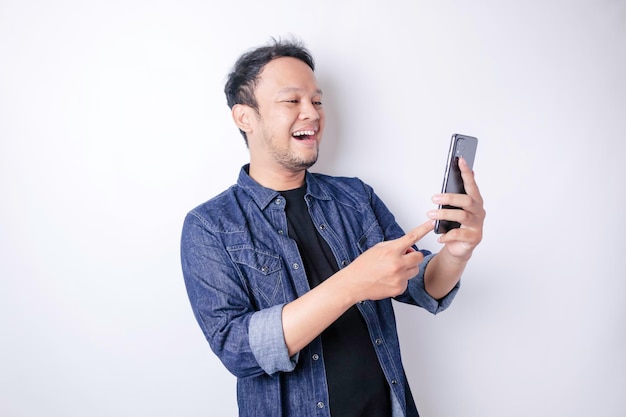 Un retrato de un hombre asiático sonriente está sonriendo y sosteniendo su teléfono inteligente con una camisa azul marino aislada por un fondo blanco