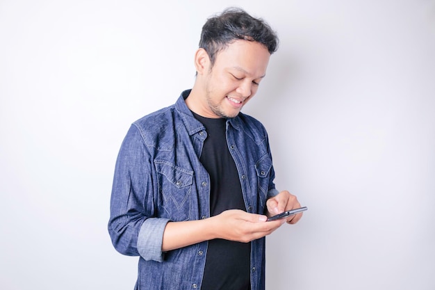 Un retrato de un hombre asiático sonriente está sonriendo y sosteniendo su teléfono inteligente con una camisa azul marino aislada por un fondo blanco