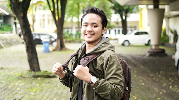 Retrato de hombre asiático sonriente con mochila de pie y mirando a la cámara