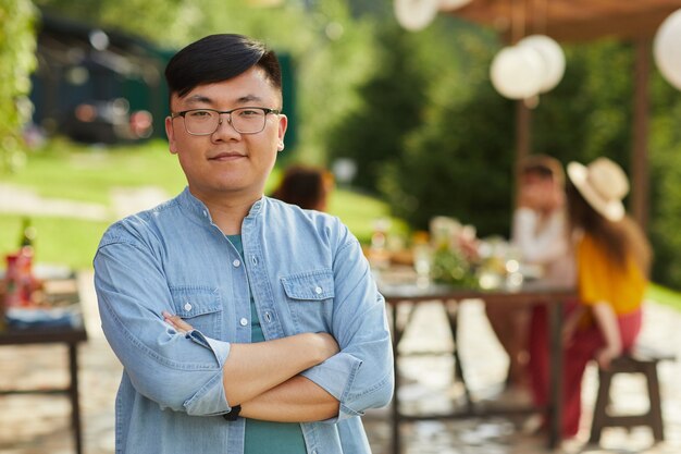 Retrato de hombre asiático sonriente posando al aire libre en verano con amigos y familiares disfrutando de una cena en la terraza