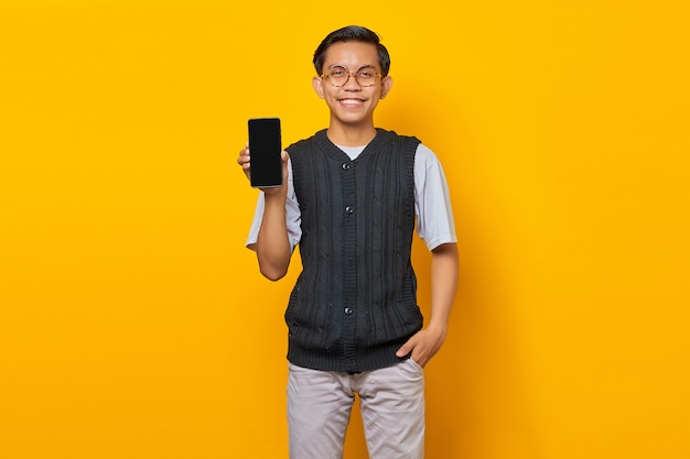 Retrato del hombre asiático sonriente que muestra la pantalla en blanco del smartphone sobre fondo amarillo