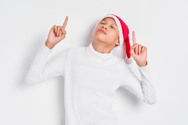 Retrato de un hombre asiático sonriente con sombrero de Navidad apuntando con el dedo hacia arriba invitando a la gente a seguir aislado de fondo blanco