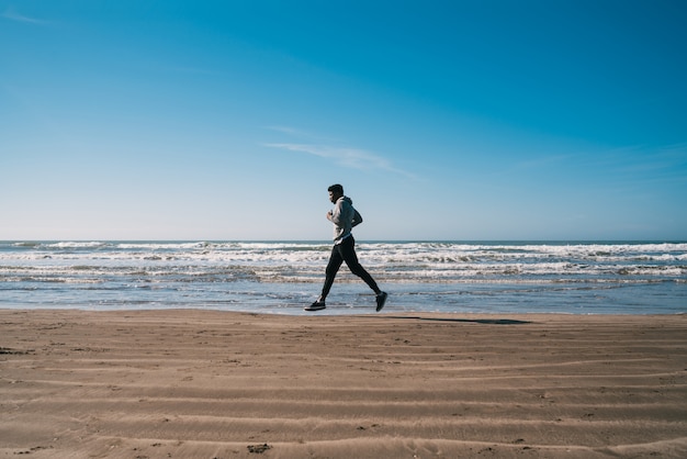 Retrato de un hombre atlético corriendo en la playa. Deporte, fitness y estilo de vida saludable.