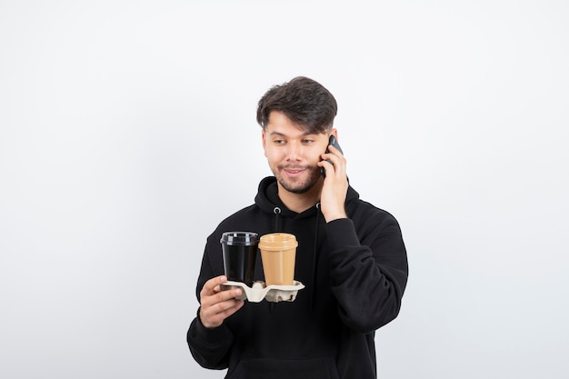 Retrato de hombre atractivo con dos tazas en una caja de cartón hablando por teléfono