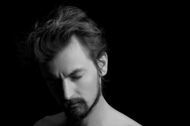 Retrato de un hombre con barba y cabello despeinado sobre un fondo negro