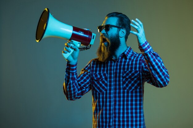 Retrato de hombre con barba hipster emocional con megáfono en el espacio en blanco en elegantes gafas de sol.