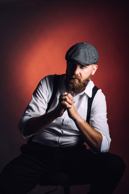 Foto retrato de un hombre barbudo con camisa blanca y tirantes sobre fondo negro en el estudio