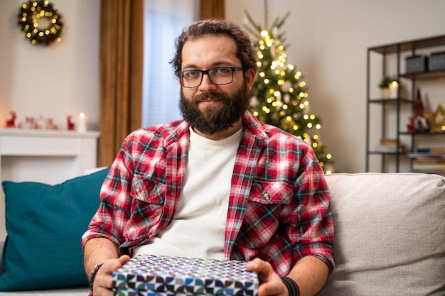 Retrato de un hombre barbudo con gafas sosteniendo una caja con un regalo de navidad recibido