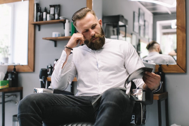 Retrato del hombre barbudo hermoso con el peinado y la barba de moda en la peluquería de caballeros.