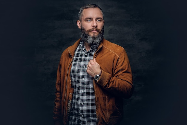 Retrato de un hombre barbudo de mediana edad vestido con una camisa a cuadros y una chaqueta de cuero marrón.