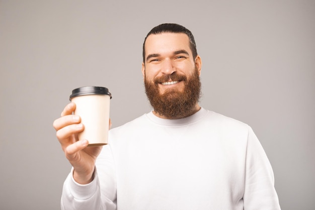 Retrato de un hombre barbudo sonriente sosteniendo y dándote una taza de café