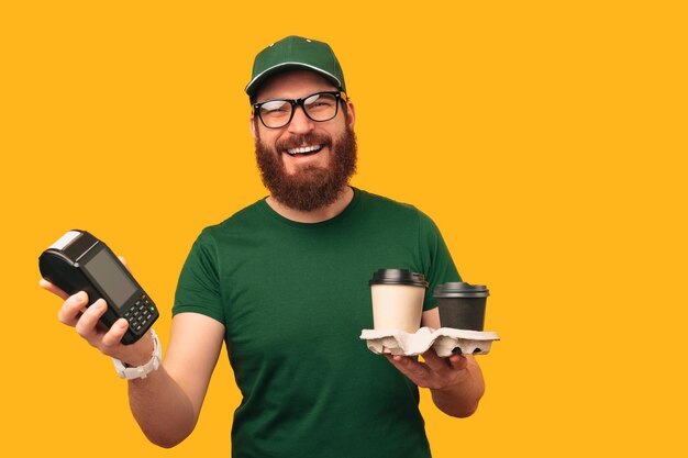 Retrato de un hombre barbudo sonriente en verde sosteniendo dos tazas y una terminal