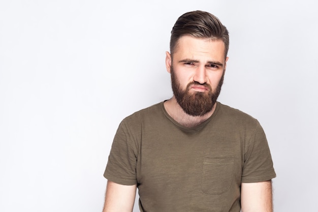 Foto retrato de hombre barbudo triste infeliz con camiseta verde oscuro sobre fondo gris claro. tiro del estudio. .