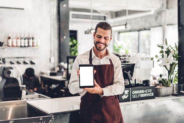 Retrato del hombre barista propietario de una pequeña empresa de pie con tablet PC con maqueta en blanco en la cafetería o cafetería en una cafetería