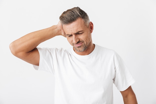 Retrato de hombre con bigote de 30 años con cerdas vistiendo camiseta casual agarrando la cabeza debido al dolor aislado en blanco