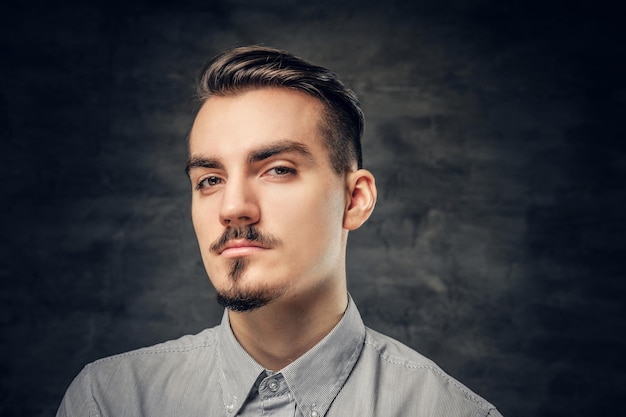 Retrato de hombre con bigote en una camisa blanca sobre fondo gris.