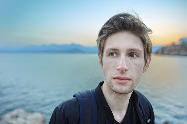 Retrato de hombre blanco triste con rasgos delicados contra el telón de fondo de la puesta del sol del mar