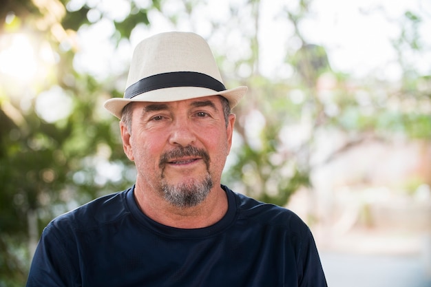 Retrato de hombre brasileño senior con sombrero blanco mirando a cámara al atardecer y sonriendo. Forma horizontal, copie el espacio.