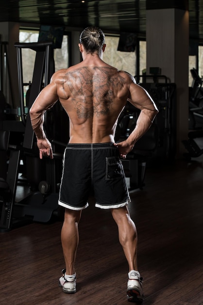 Retrato de un hombre en buena forma física en el moderno gimnasio mostrando poses traseras